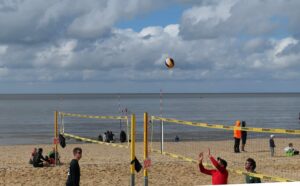players volleying a volleyball on a beach volleyball court with lake in the background