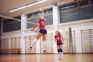 female volleyball player hitting the ball with the setter looking on