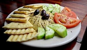 pita crackers, hummus, sliced tomatoes and sliced cucumbers on a plate