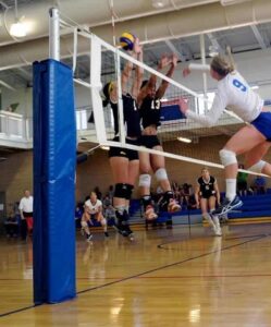 female volleyball player hitting the ball with two blockers across the net