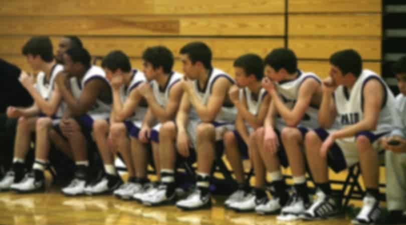 male basketball players sitting on a bench, focused on the game