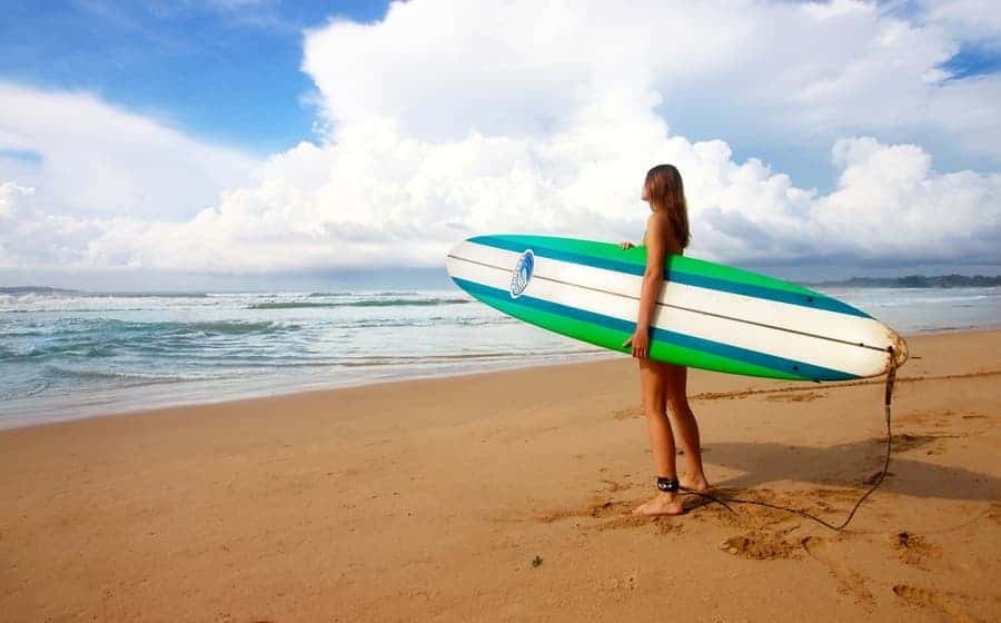 woman standing on beach holding a surfboard watching the waves