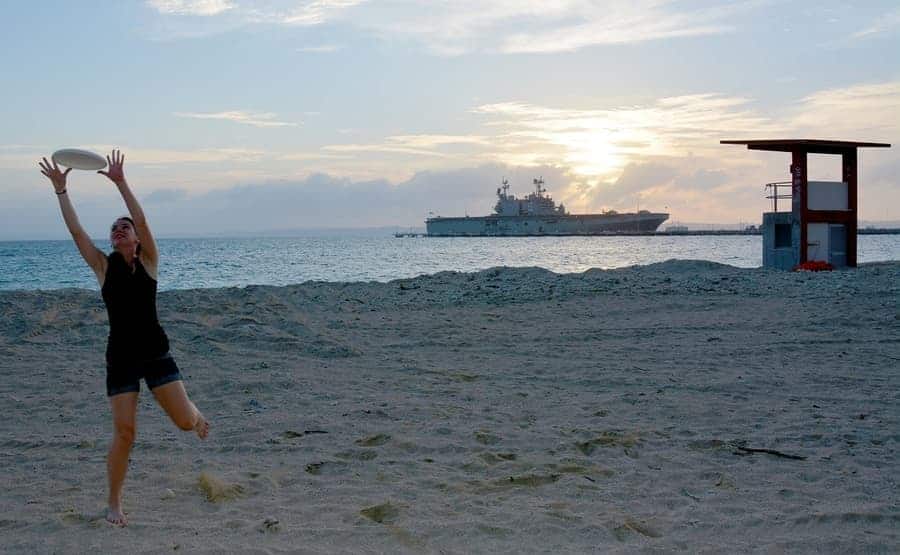 girl playing frisbee on beach with ocean liner in the background