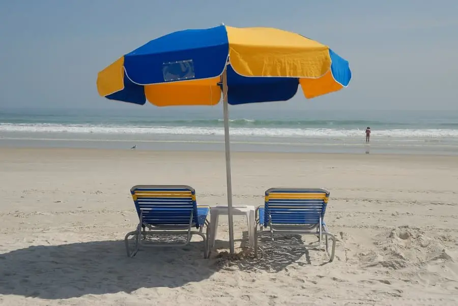 two beach chairs under umbrella on the sand with beach in the background