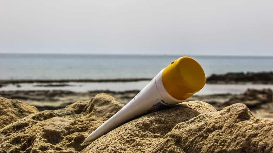 tube of sunscreen laying on sand with beach in the background