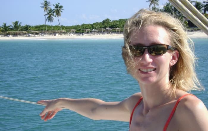 blonde woman wearing sunglasses with beach shoreline in the background