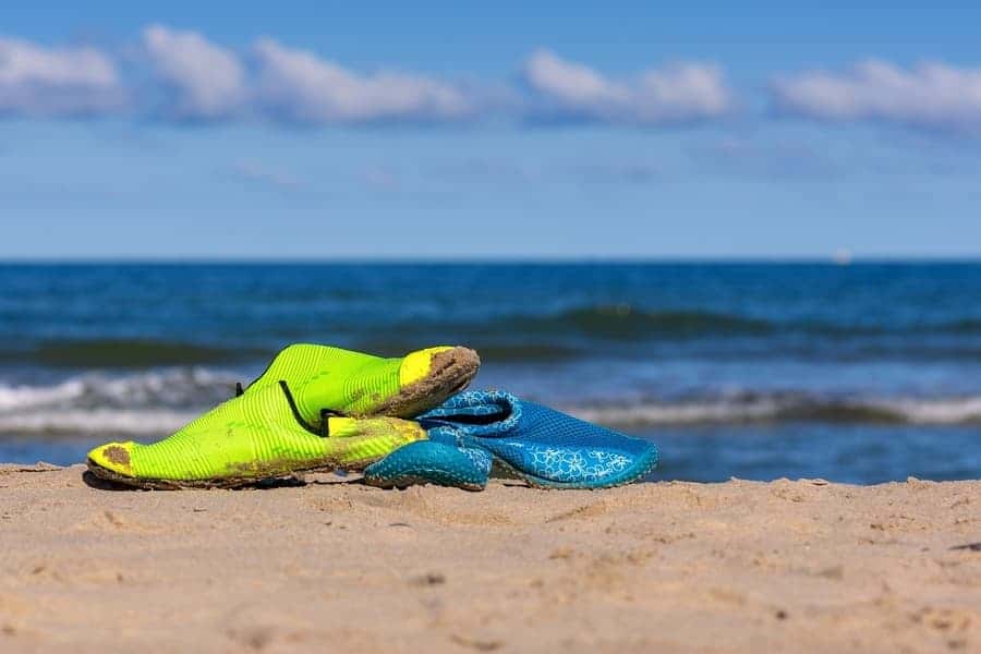 two pairs of water shoes sitting on the sand with water in the background