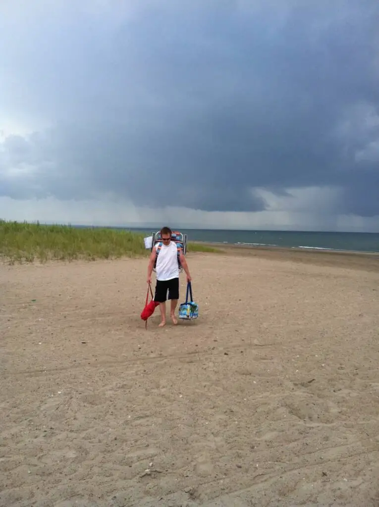 man walking on the beach, carrying beach supplies, with storm breaking in the background