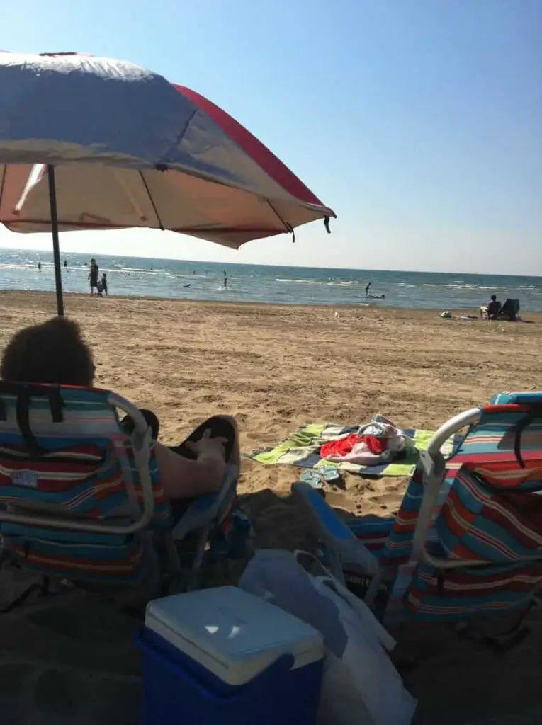 man relaxing on the beach, sitting in a beach chair under an umbrella and looking at the water