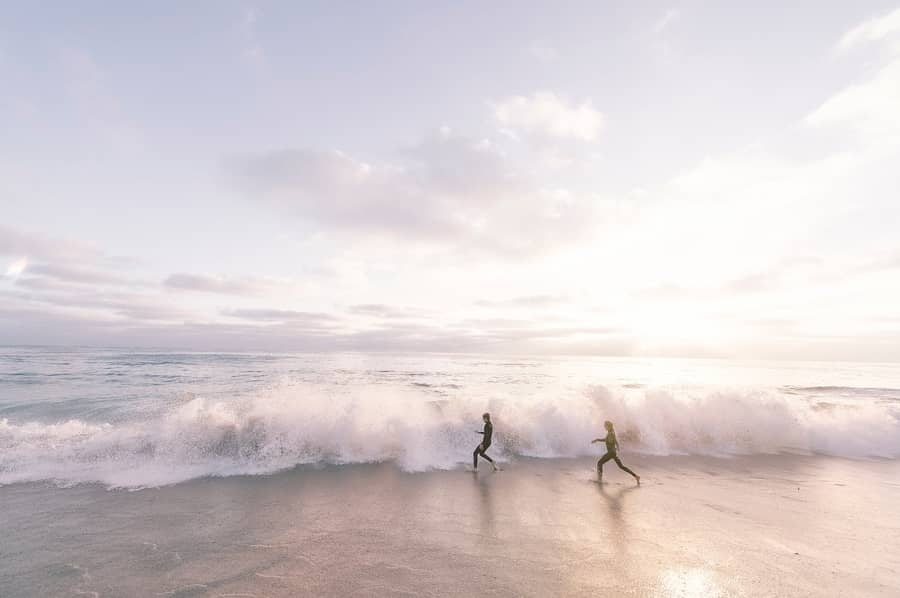 two people running on the beach into breaking waves