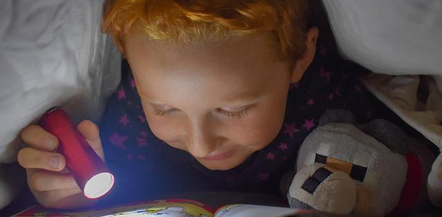 Kid reading a book under a blanket